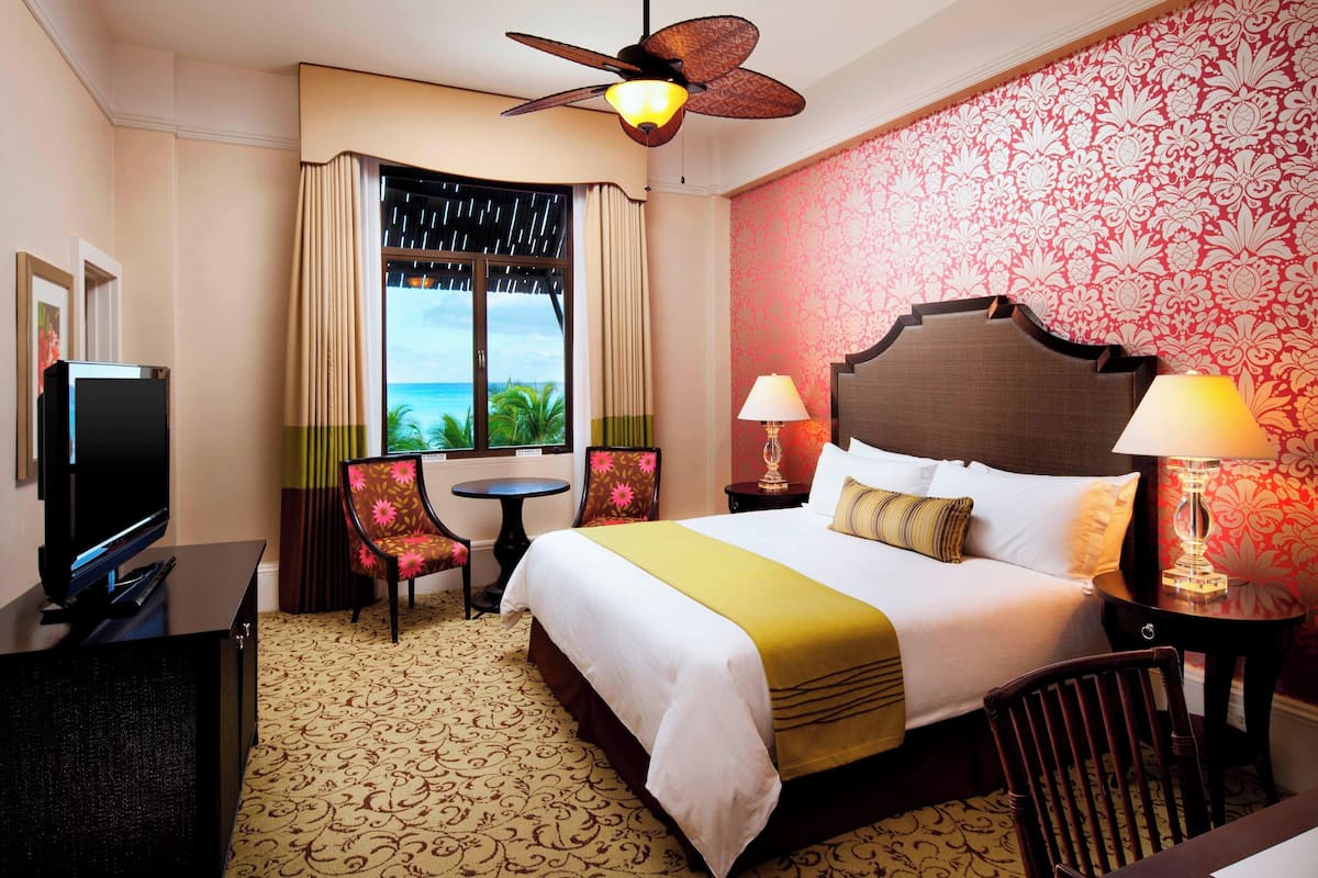 A hotel room with a bed, a television, a desk, a chair, and a view of the ocean.