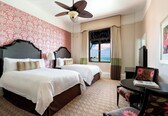 A hotel room with two beds, a ceiling fan, a view of the ocean, and a dining area with a table and chairs.