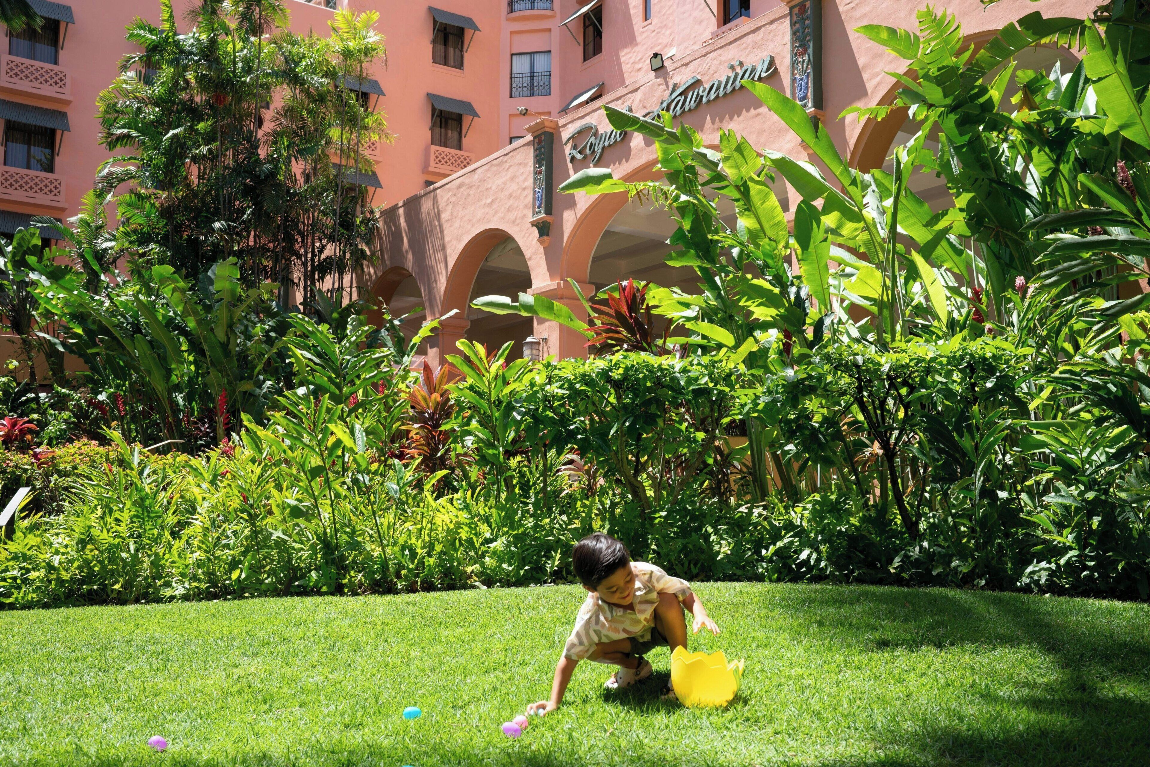 A child playing in a lush garden area with a building in the background.