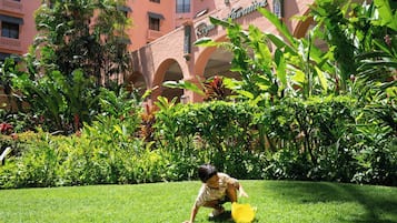 A child playing in a lush garden area with a building in the background.