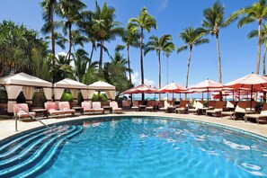 Relax by the tranquil pool surrounded by palm trees and lounge chairs.