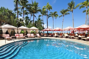 Relax by the tranquil pool surrounded by palm trees and lounge chairs.