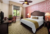 A hotel room with a large bed, two bedside lamps, a ceiling fan, a TV, and a desk with a chair.