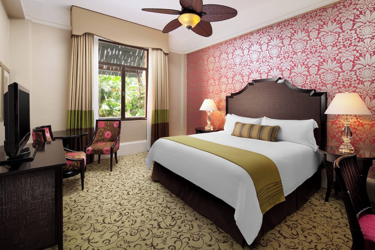 A hotel room with a large bed, two bedside lamps, a ceiling fan, a TV, and a desk with a chair.