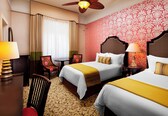 A hotel room with two beds, a desk, a chair, and a ceiling fan.
