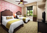 A hotel room with two beds, a ceiling fan, a television, and a window with curtains.