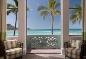 A room with a view of the ocean and palm trees, featuring two striped armchairs and a decorative screen.