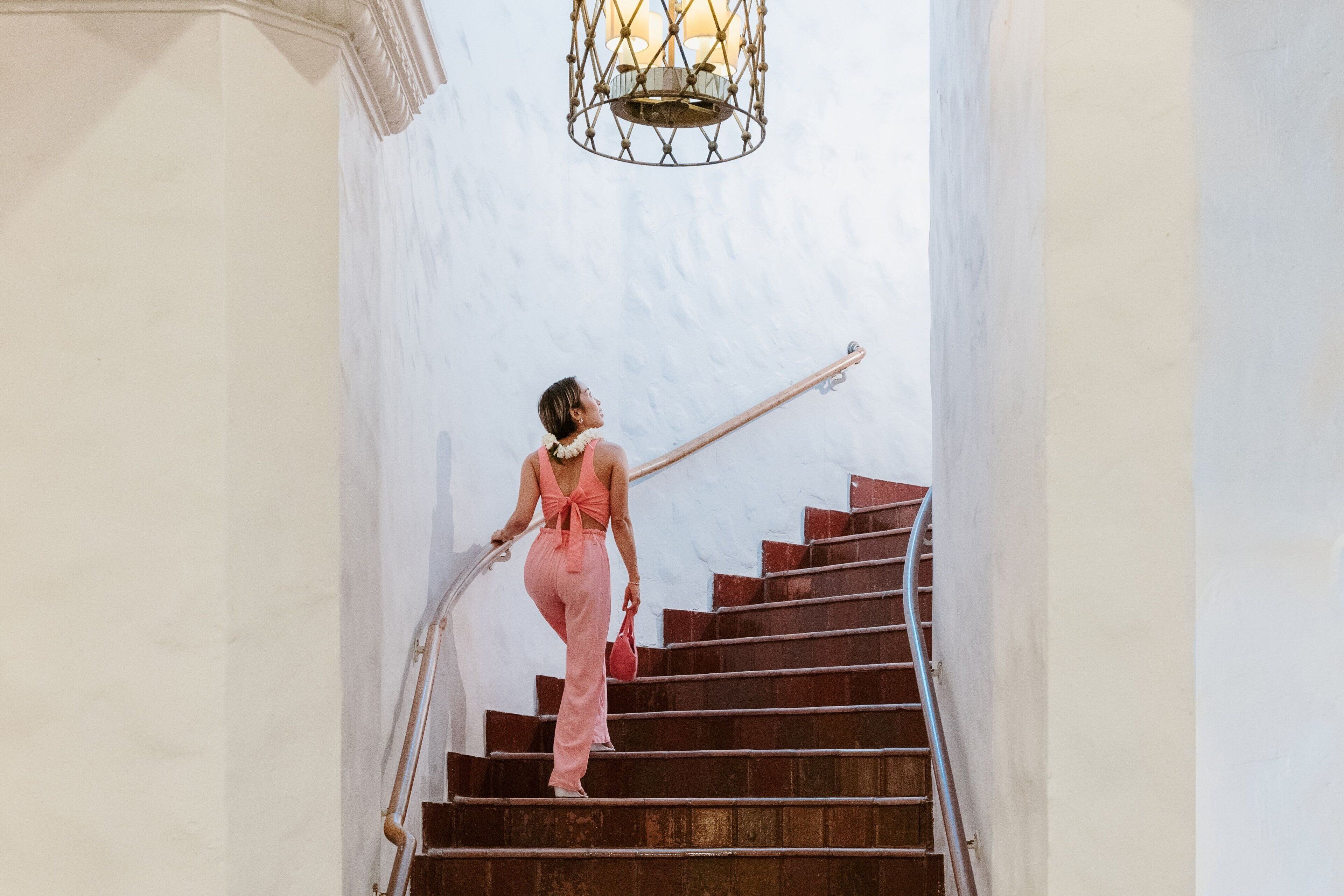 A person descending a staircase with a metal railing, white walls, and a hanging light fixture.