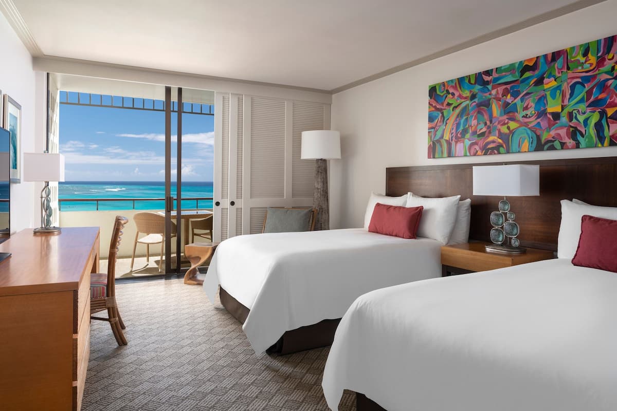 A hotel room with two beds, a desk, a chair, a large window with a view of the ocean, and a colorful abstract painting on the wall.