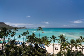 A beach with clear turquoise waters, palm trees, and beach umbrellas.