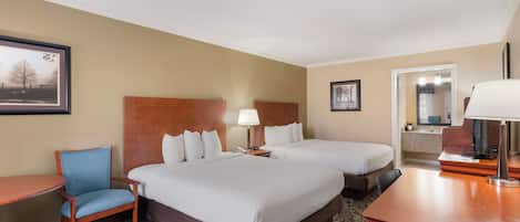 A hotel room with two beds, a desk, a chair, a lamp, and a framed picture on the wall.