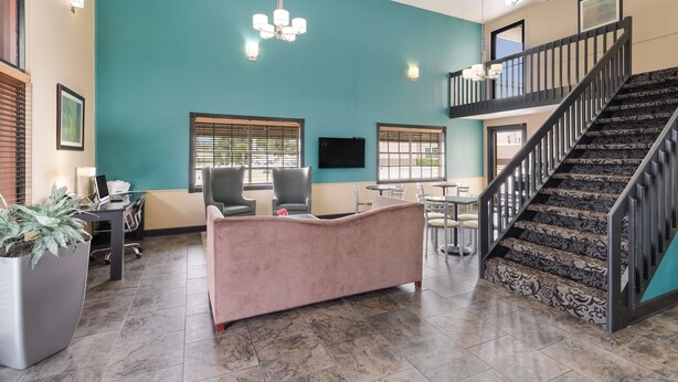 A spacious lobby with a teal accent wall, a pink sofa, a staircase with patterned carpet, and a dining area with tables and chairs. - Best Western Conway (Conway)
