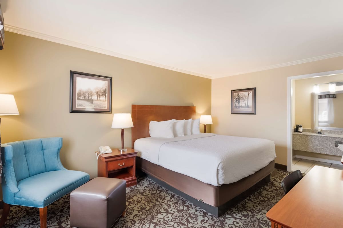 A hotel room with a bed, a chair, a desk, and a bathroom visible through an open door.