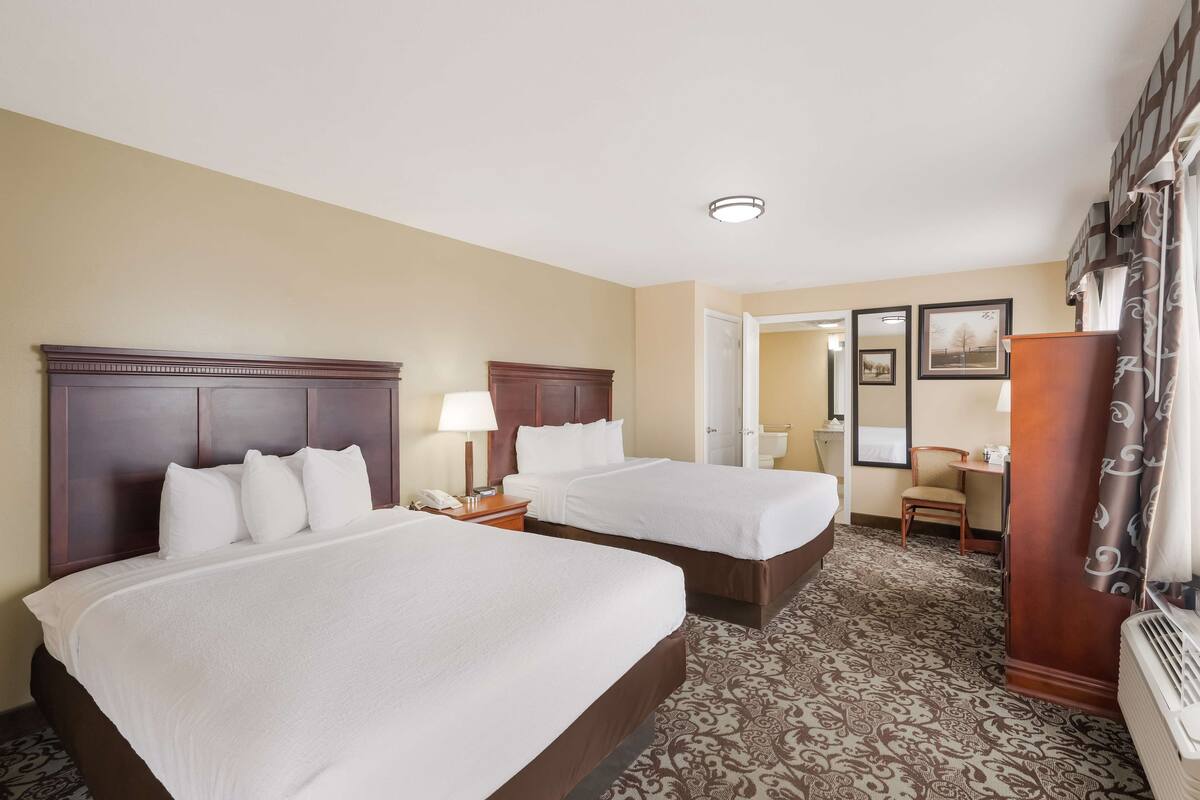 A hotel room with two beds, a desk, a chair, a mirror, and a door leading to another room.