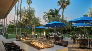 An outdoor patio area with a fire feature, dining tables, chairs, and blue umbrellas. - Torrance Marriott Redondo Beach (Torrance)