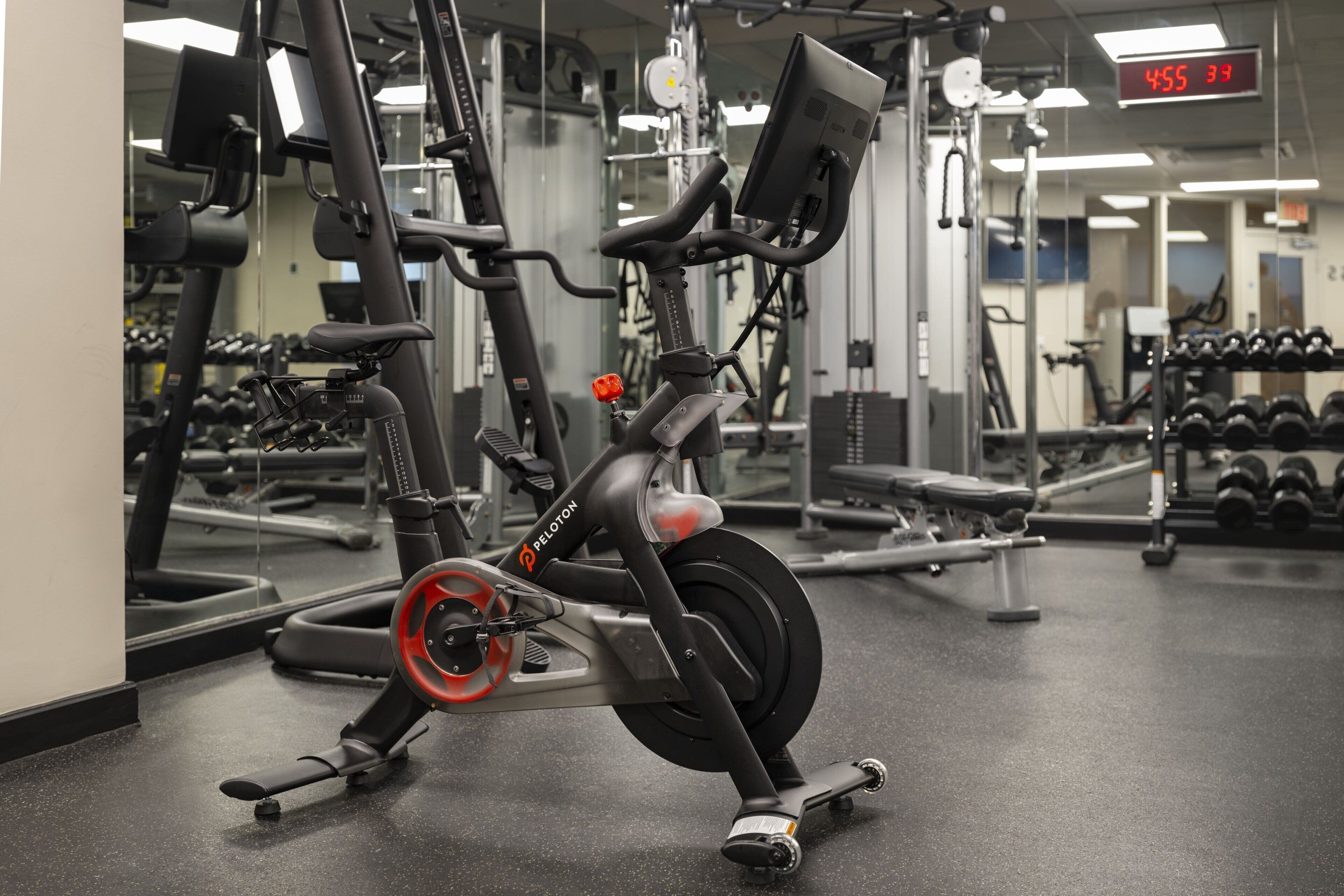 Un vélo d’appartement doté d’un écran numérique, du matériel de musculation et un porte-haltères dans une salle de sport.