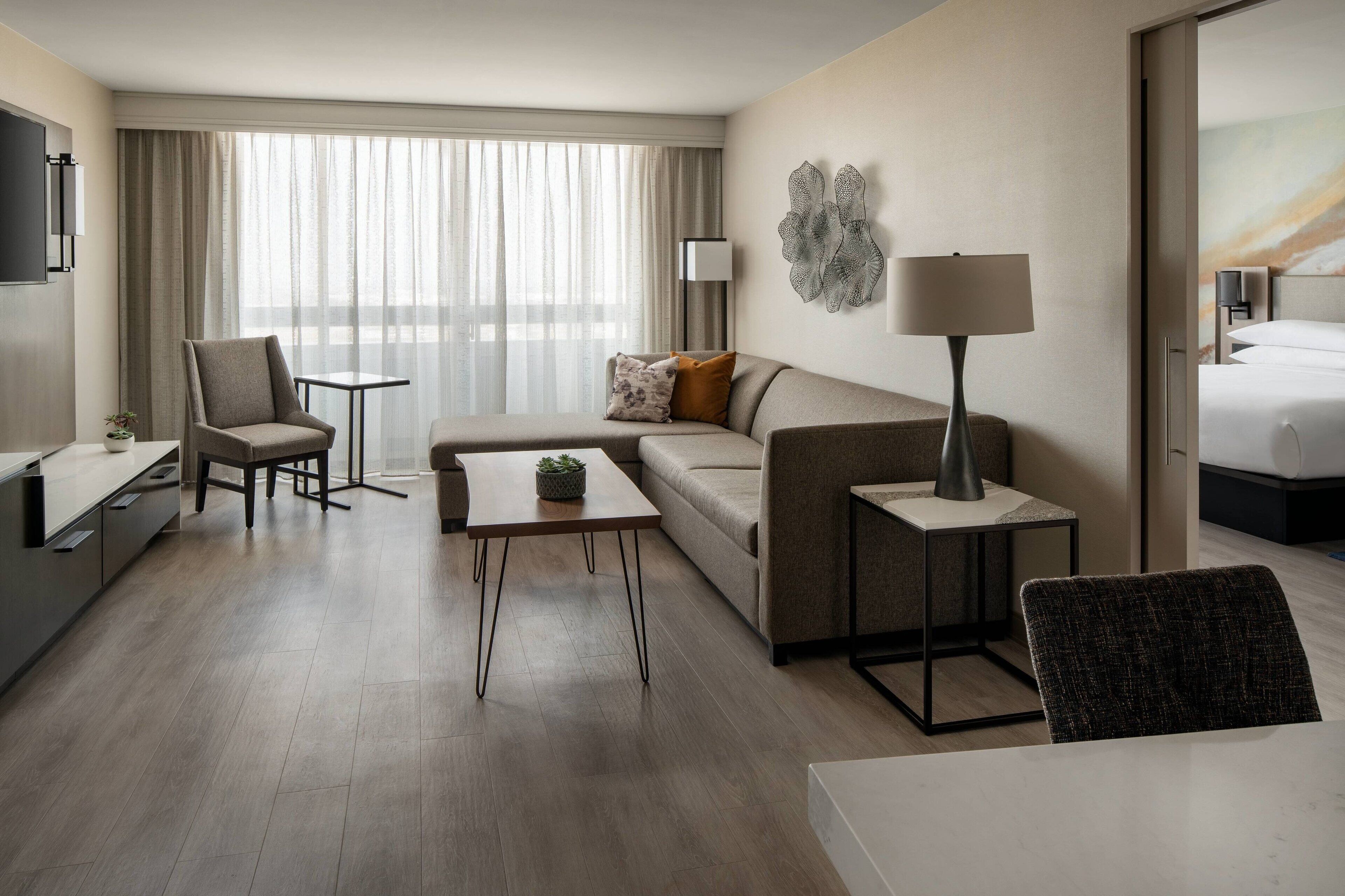A modern hotel room with a sofa, armchair, coffee table, and a bed.