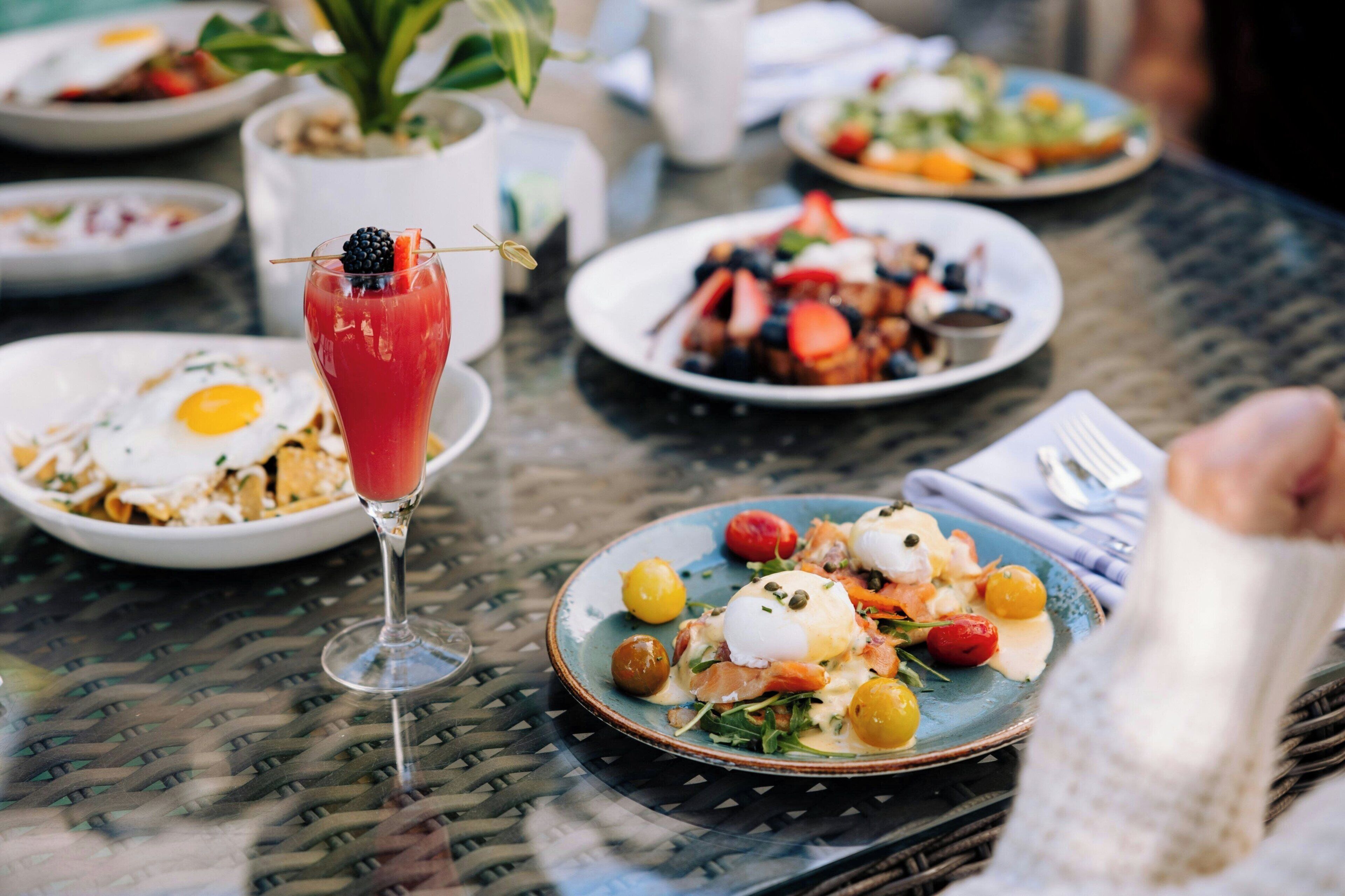 Une table à manger avec différents plats, notamment des œufs, une salade et un verre d’une boisson rouge.