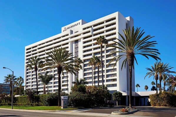Un hotel Marriott de varios pisos con un diseño moderno, rodeado de palmeras y jardines bien cuidados.