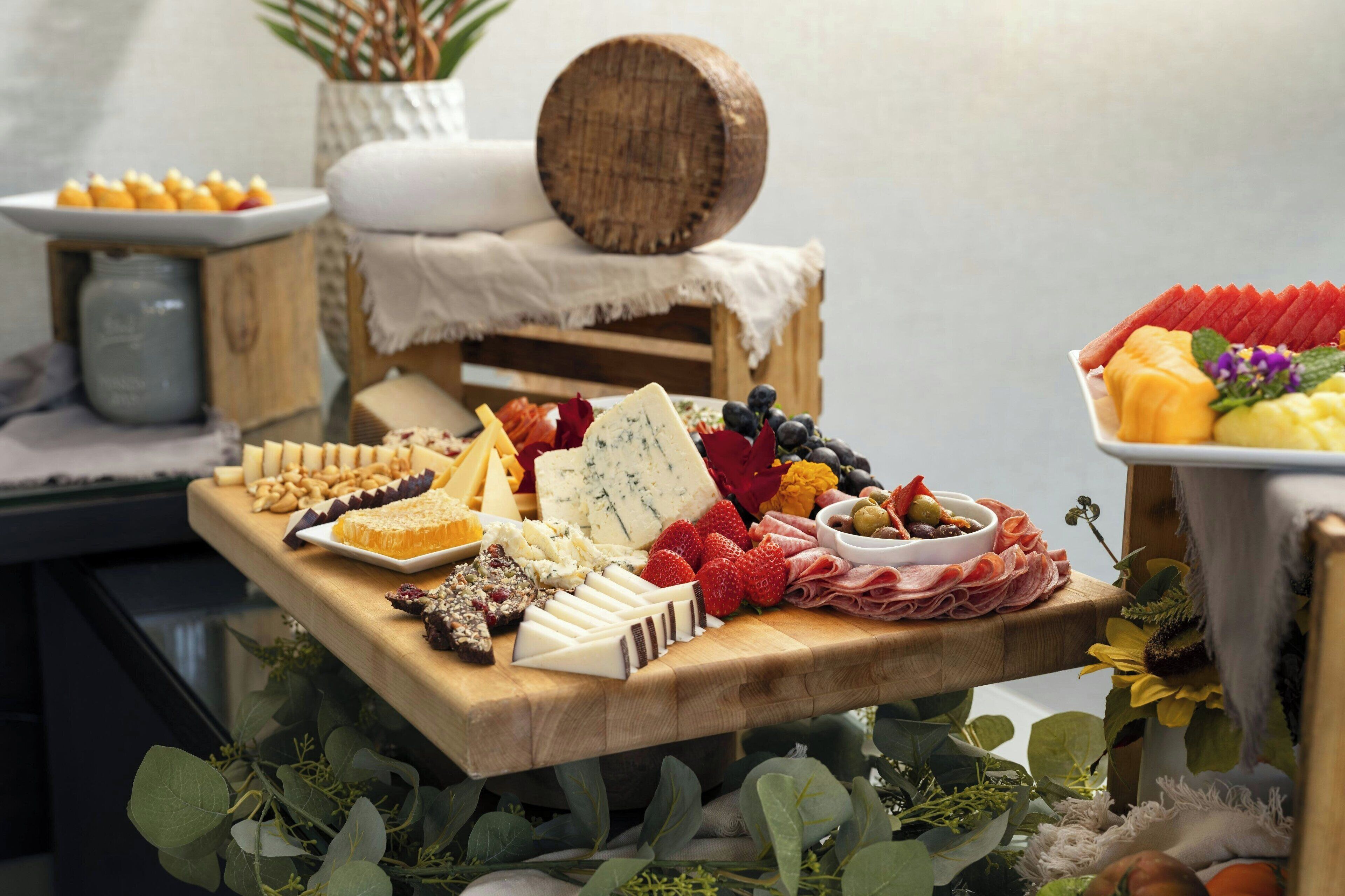 Une planche en bois servant de présentoir, sur laquelle sont disposés différents fromages, des fruits et des charcuteries.