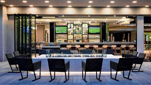 An outdoor bar area with a long counter, multiple bar stools, and a television screen displaying a sports game. - Torrance Marriott Redondo Beach (Torrance)