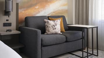 Una sala moderna con un sofá gris, una mesita auxiliar, una lámpara de pared y un cuadro abstracto grande.