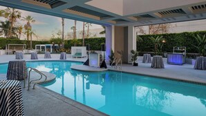 A modern indoor pool area with lounge chairs, a bar, and a view of palm trees. - Torrance Marriott Redondo Beach (Torrance)