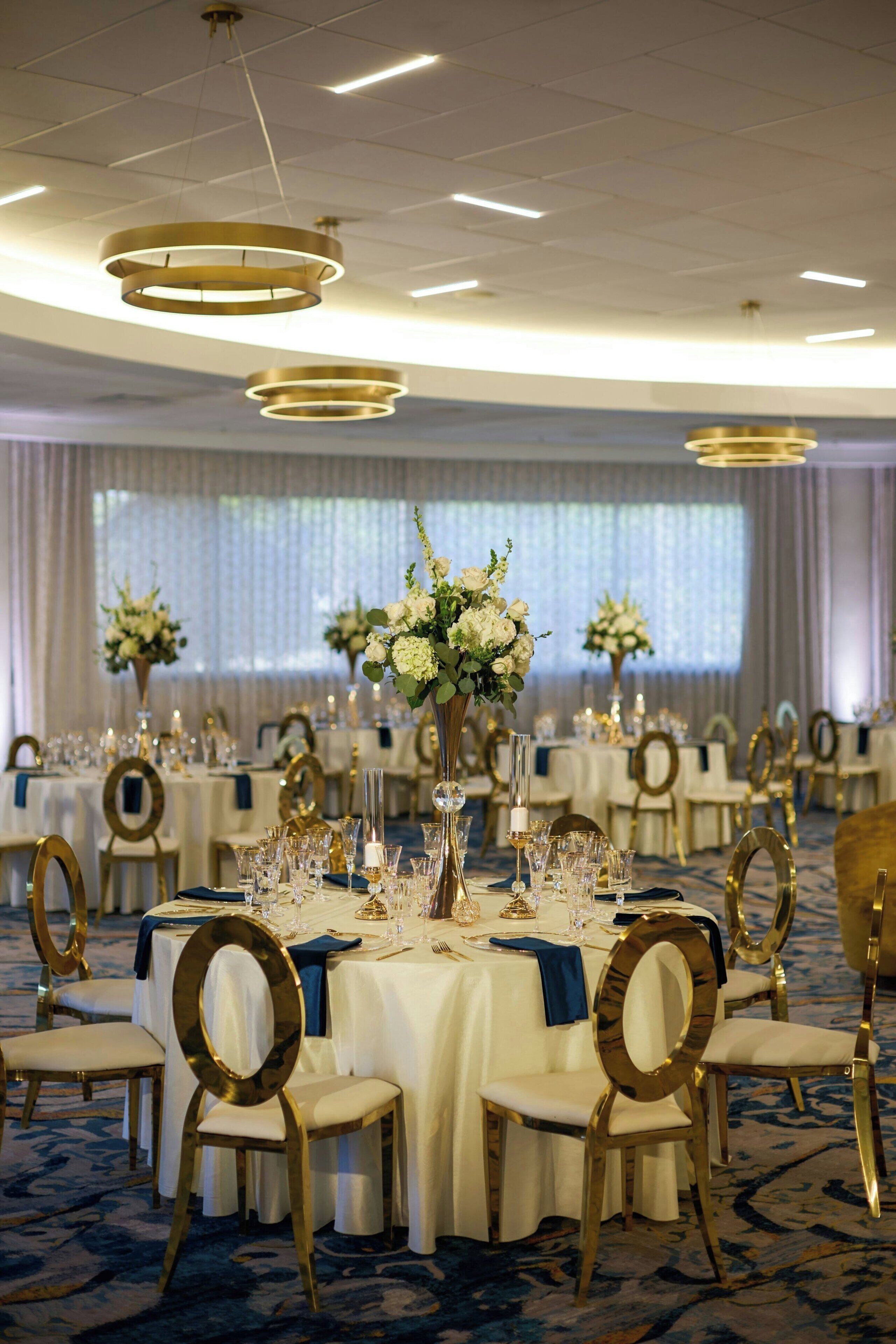 A banquet hall with round tables, gold chairs, and floral centerpieces.