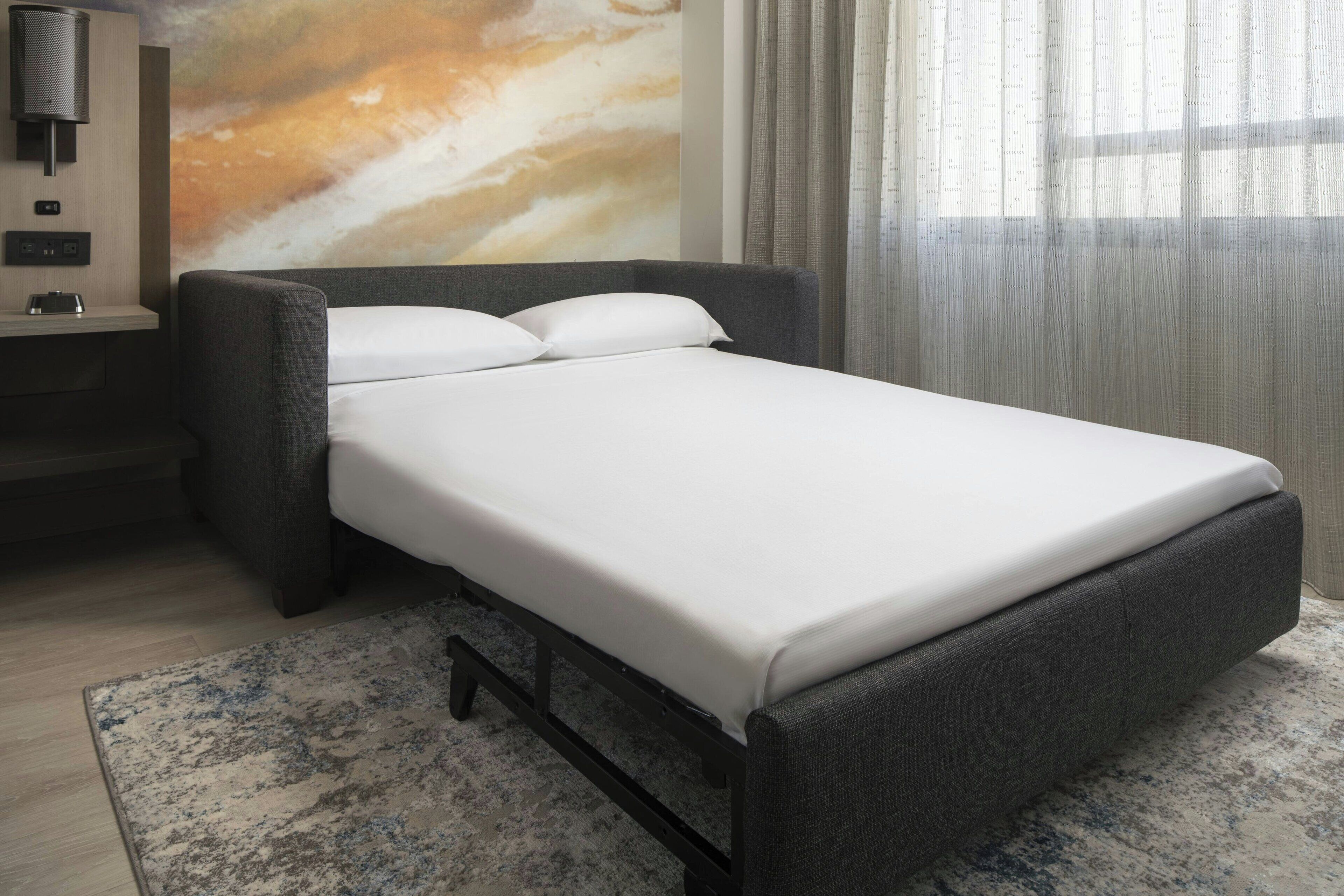 A modern hotel room with a single bed, a bedside table with a lamp, and a large abstract wall mural.