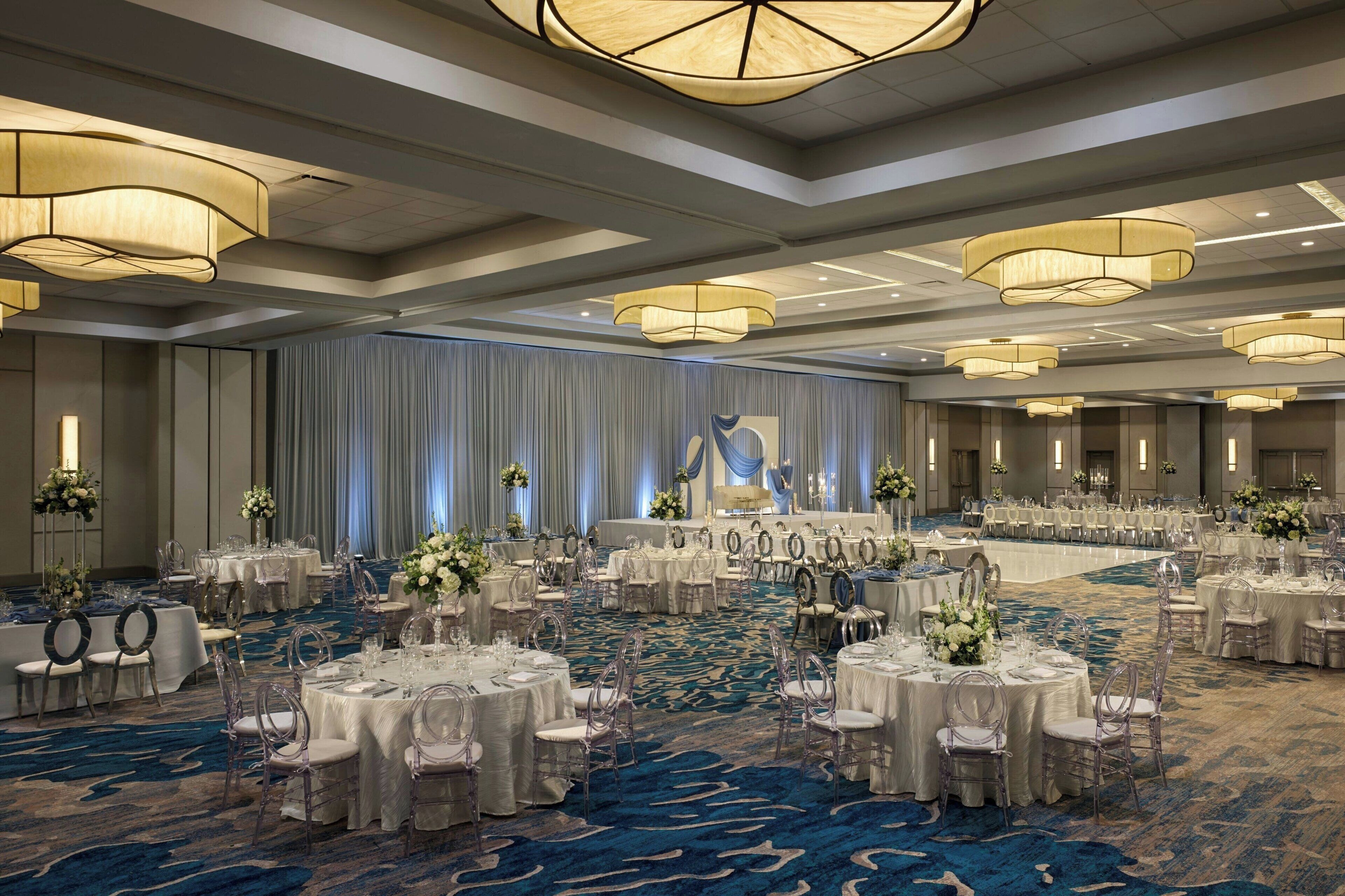 Une grande salle de banquet avec des tables rondes, des chaises et une scène.