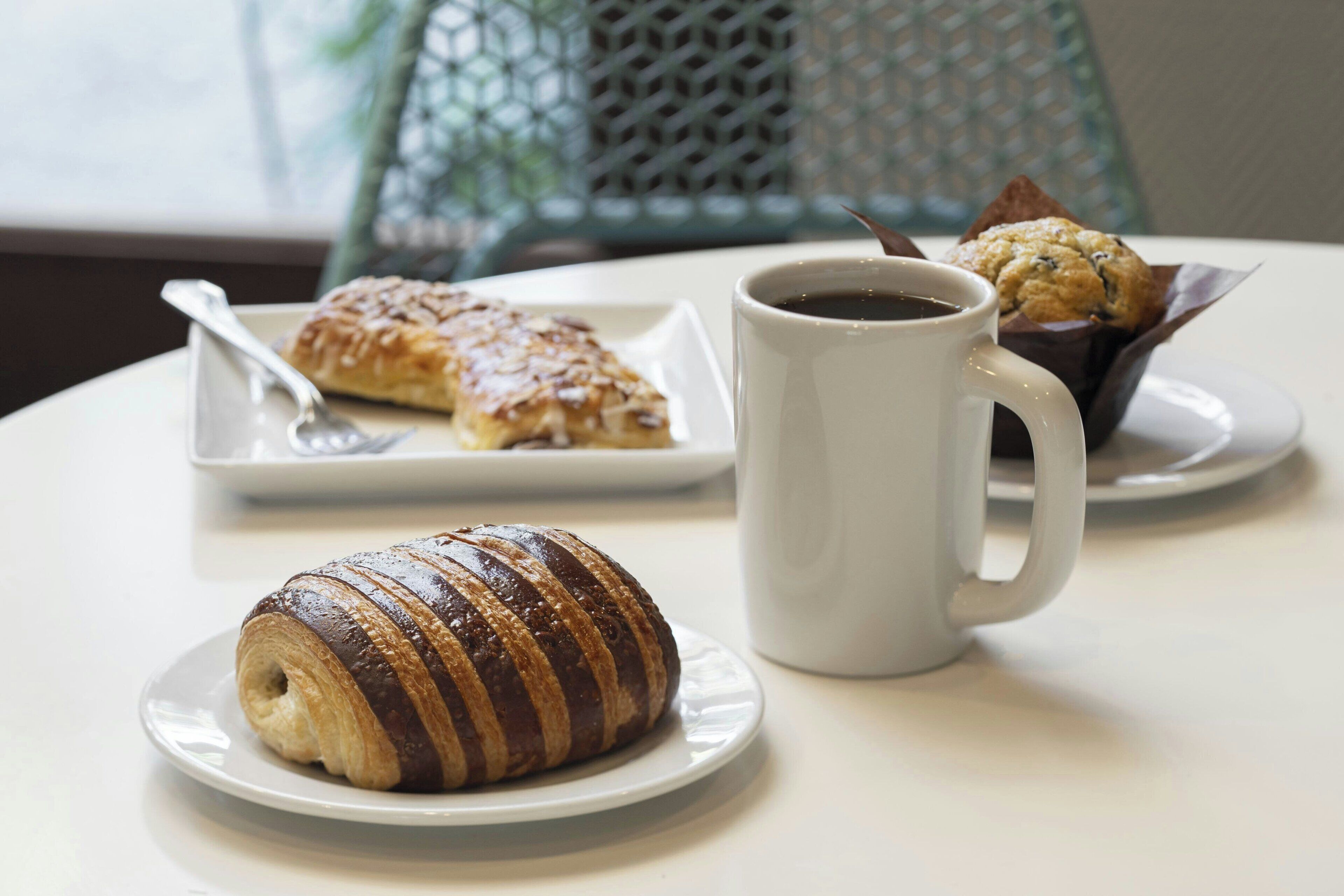 En croissant, en muffin och en kopp kaffe på ett bord.