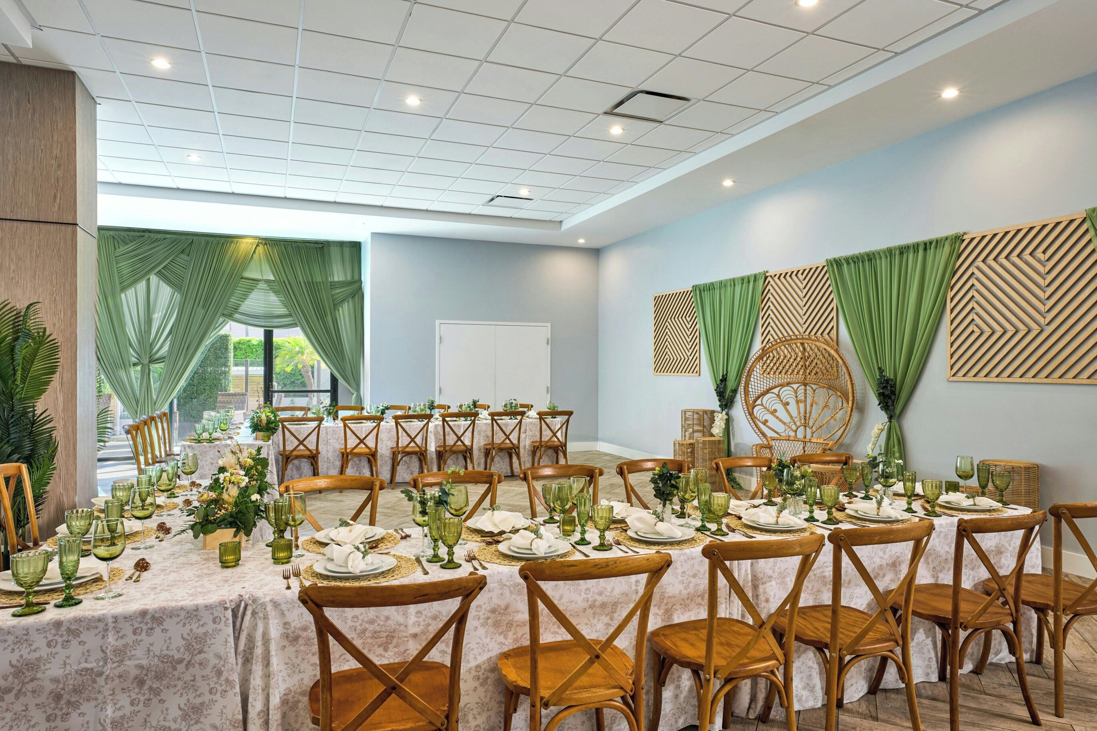 Un salón de conferencias con varias mesas dispuestas para comer, sillas de madera y un amplio ventanal con cortinas.