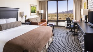 A hotel room with a large bed, a desk with a computer, a chair, and a view of the desert through large windows. - Kayenta Monument Valley Inn (Kayenta)