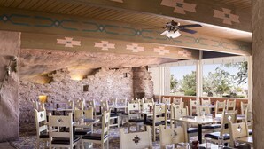 A restaurant with rustic stone walls, wooden ceiling, and patterned floor tiles. Tables and chairs are arranged for dining. - Kayenta Monument Valley Inn (Kayenta)