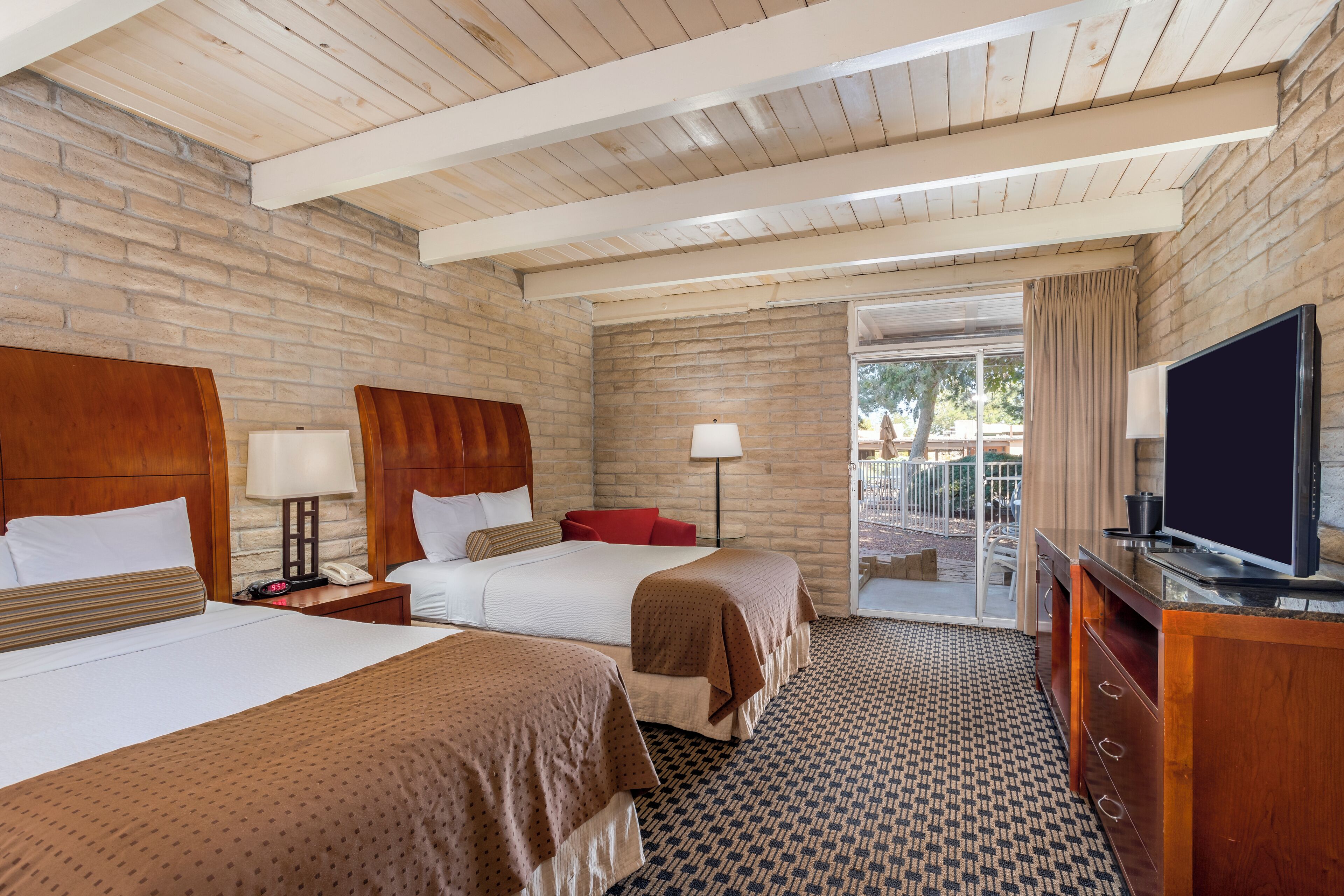 A hotel room with two beds, a TV, a desk, and a balcony with a view.