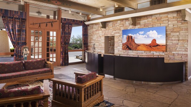 A lobby with a reception desk, a large painting of a desert landscape, and a seating area with patterned cushions. - Kayenta Monument Valley Inn (Kayenta)