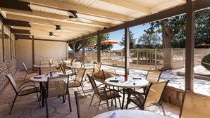An outdoor patio area with round tables and chairs, umbrellas, and a view of the ocean. - Kayenta Monument Valley Inn (Kayenta)