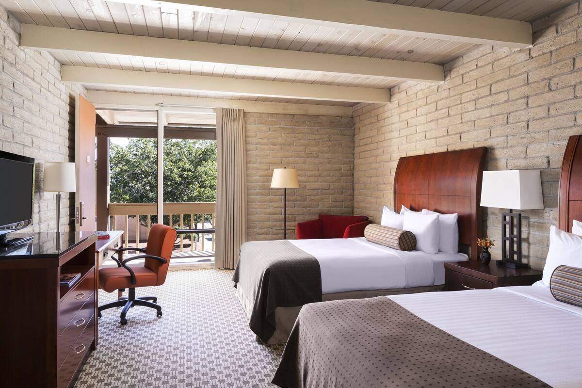 Une chambre d’hôtel avec un mur en briques, deux lits, un bureau avec une chaise et un téléviseur.