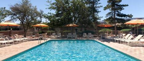 A rectangular swimming pool with clear blue water, surrounded by lounge chairs and orange umbrellas.