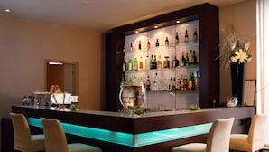 A bar area with a long counter, multiple shelves of liquor bottles, and two bar stools. - Hotel De Fierlant (Brussels)