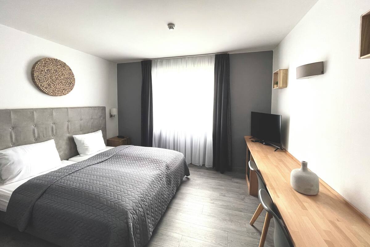 A modern hotel room with a large bed, a wooden desk, a flat-screen TV, and a round wall decoration.