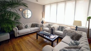 A living room with a sofa set, a coffee table, a lamp, and a large plant. - Hotel De Fierlant (Brussels)