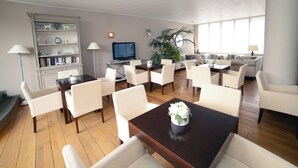 A spacious living area with a wooden floor, white furniture, a bookshelf, a television, and a large window providing natural light. - Hotel De Fierlant (Brussels)
