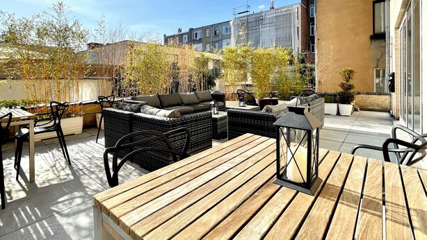 An outdoor patio with wicker furniture, a wooden table, and potted plants. - Hotel De Fierlant (Brussels)
