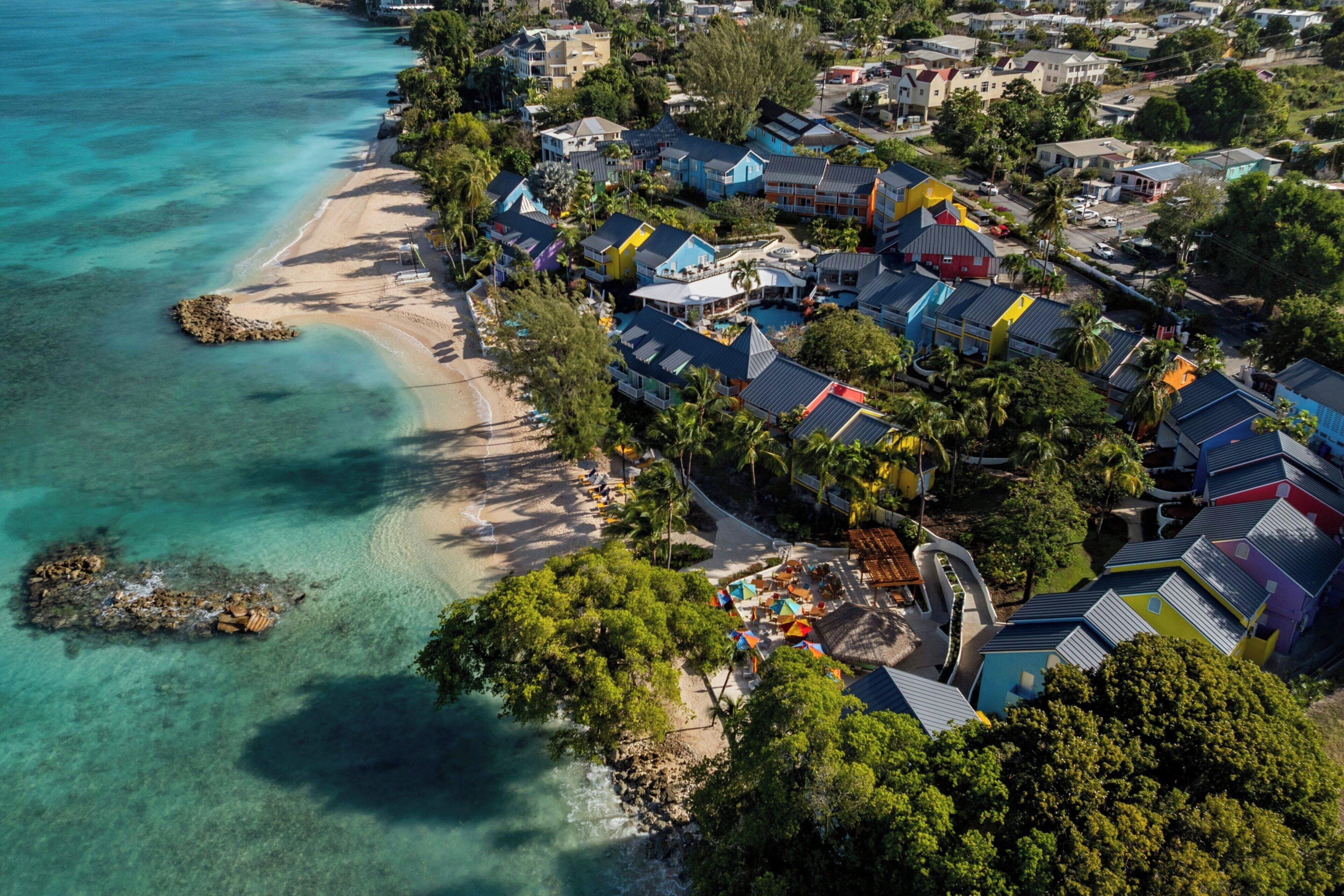 An aerial view of a coastal resort with beachfront properties, clear turquoise waters, and lush greenery.