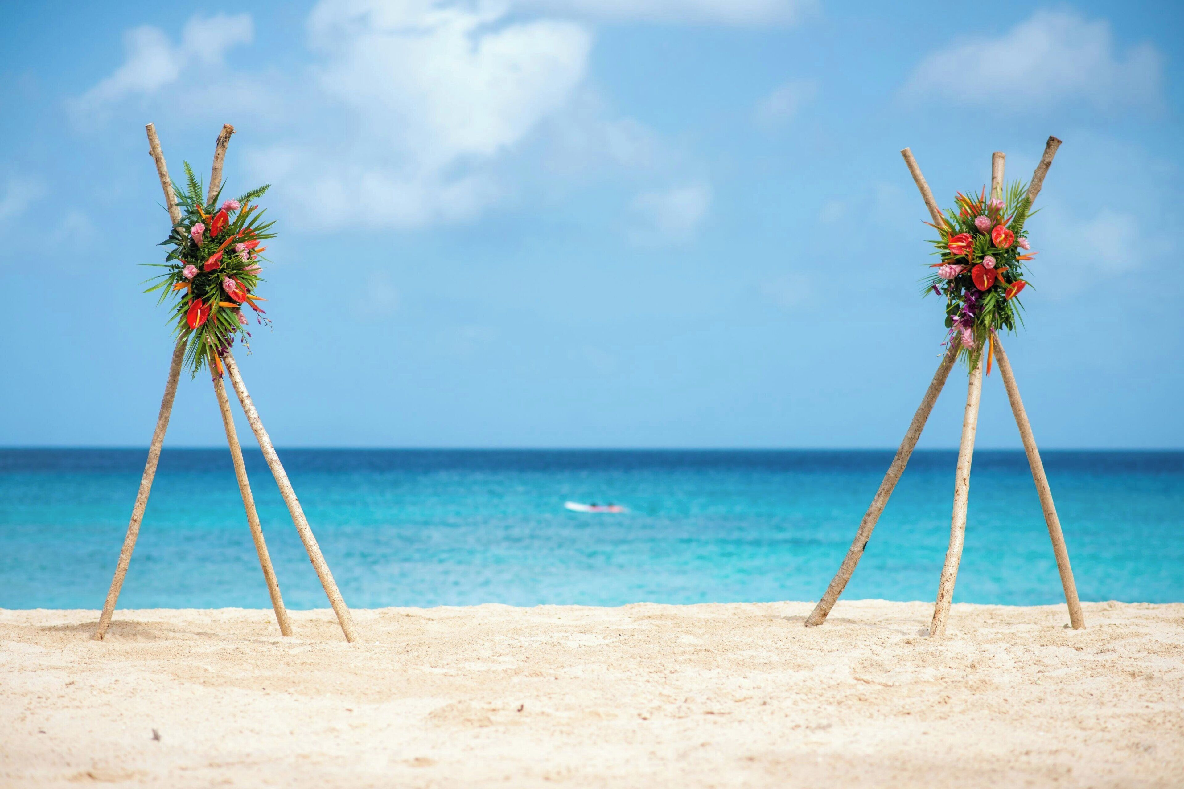 A beach with two wooden stands holding floral arrangements against a clear sky and ocean backdrop.