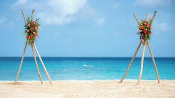 A beach with two wooden stands holding floral arrangements against a clear sky and ocean backdrop.