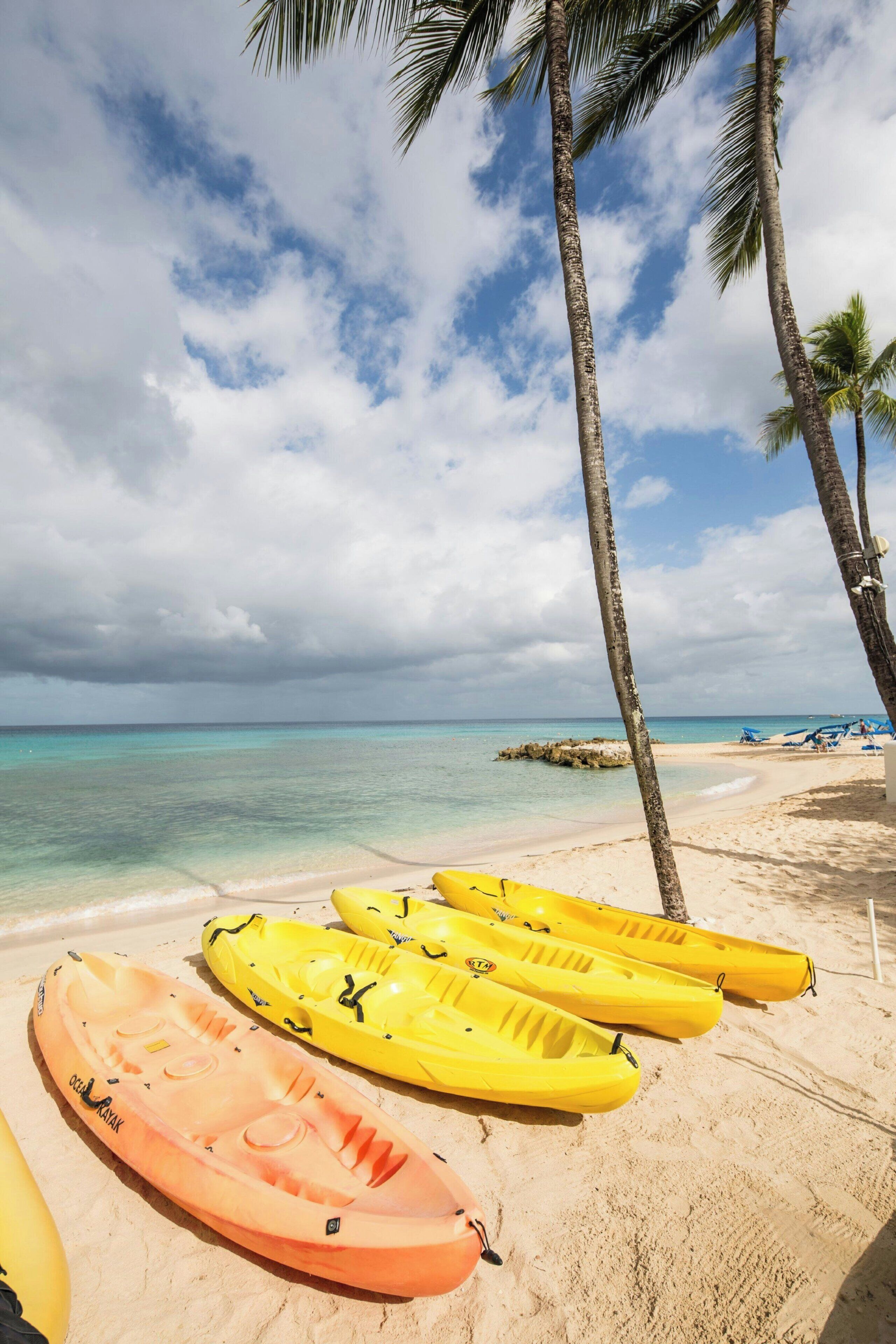 A beach with kayaks, palm trees, and a clear sky.