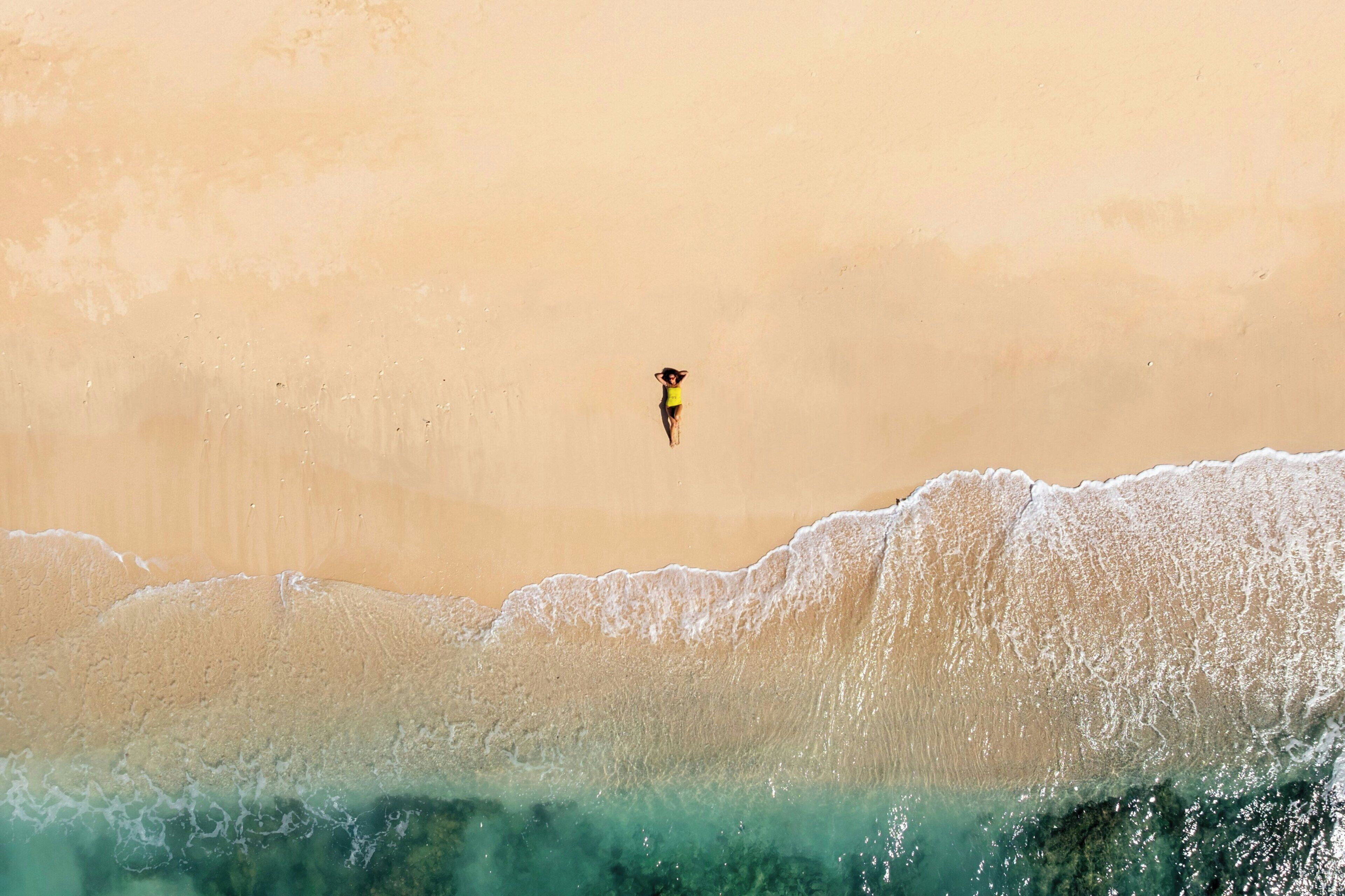 A beach scene with a person standing on the sand near the water's edge.