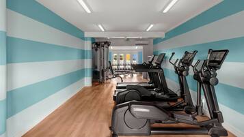 A gym with exercise equipment, a wooden floor, and teal-striped walls.